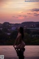 A woman sitting on the edge of a swimming pool at sunset.