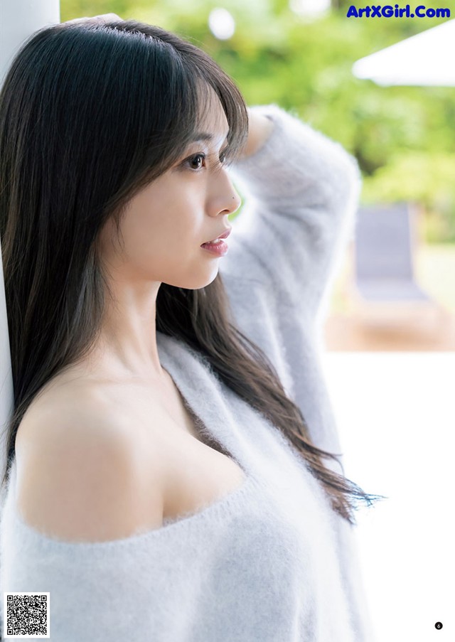 A woman with long black hair leaning against a wall.